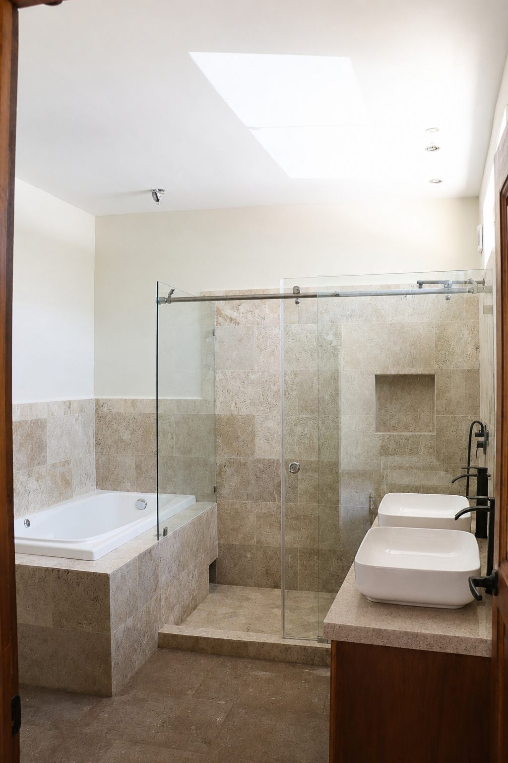 Bathroom with travertine finishes, glass shower and double sinks under a skylight