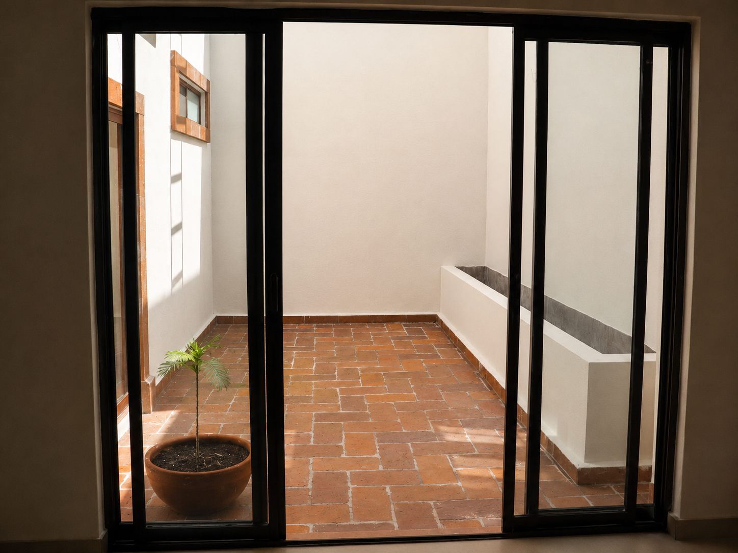 Interior patio with terracotta floors seen through black-framed glass doors